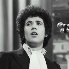 Lucio Battisti, con la sua iconica chioma, canta "Il tempo di morire" davanti a un microfono.
