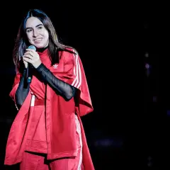 Federica Abbate canta sul palco, sorridente, con un outfit rosso Adidas. I suoi amici la guardano con ammirazione.