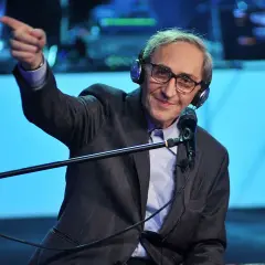 Franco Battiato, con cuffie e microfono, indica con il dito, come in un "auto da fé" di parole.