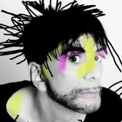 Ritratto di Ivan Cattaneo con capelli neri a punta, trucco colorato e barba. Le sue canzoni sono uniche.