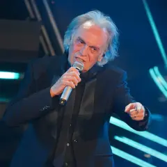 Riccardo Fogli canta sul palco, con il microfono in mano, evocando le sue indimenticabili canzoni.