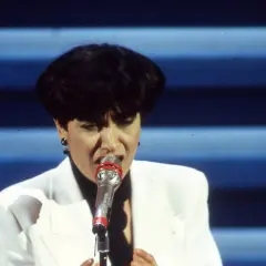 Mia Martini, icona della musica italiana, canta con passione sul palco, illuminata da luci soffuse.