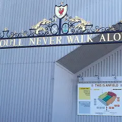 L'iconico cancello di Anfield con la scritta "You'll Never Walk Alone" e lo stemma del Liverpool. Un simbolo di unità e passione.