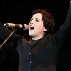 Dolores O'Riordan, iconica voce dei The Cranberries, canta con passione sul palco, braccia alzate in un momento di pura energia.