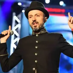 Un cantante con cappello e giacca nera, microfono in mano, evoca le canzoni dei Subsonica con un gesto energico.