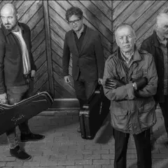 I membri di the Animals, quattro uomini con valigie per strumenti musicali, posano davanti a un portone di legno.