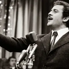 Domenico Modugno, originario di Polignano a Mare, canta con passione al microfono, con il braccio teso.