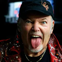 Vasco Rossi, con la lingua fuori e un'espressione grintosa, indossa una giacca borchiata. Chissà quante canzoni ha fatto Vasco Rossi per arrivare a tanta energia!