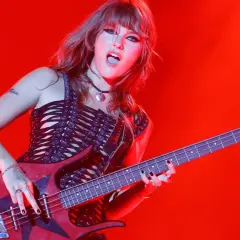Victoria De Angelis, bassista dei Måneskin, suona con passione sul palco, illuminata da luci rosse.