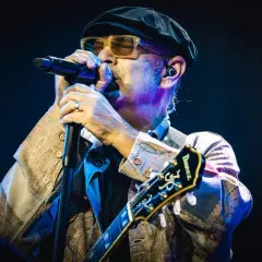 Luca Carboni canta "Le storie d'amore" con passione, chitarra in mano, sotto le luci del palco.