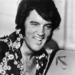 Un giovane Elvis Presley, con la sua iconica capigliatura e una camicia floreale, sorride. Un'immagine che cattura un momento della sua storia.