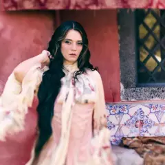 Carmen Consoli, con lunghi capelli scuri e un abito etereo, posa con un'espressione intensa. L'ambientazione ricorda un cortile con piastrelle decorative, evocando un'atmosfera da "Orfeo".