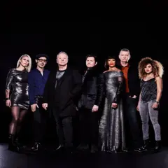 I membri dei Simple Minds posano in gruppo su sfondo nero, vestiti con abiti eleganti e scintillanti.