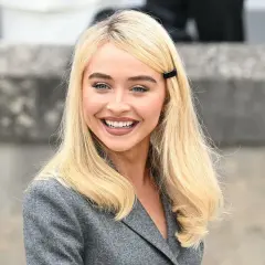 Sabrina Carpenter sorride, con i capelli biondi e un blazer grigio. Ricorda i suoi film e programmi TV.