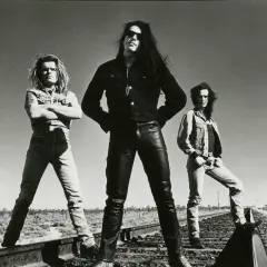 I membri dei The Cult posano sulle rotaie in un paesaggio desertico, con un cielo limpido sullo sfondo.