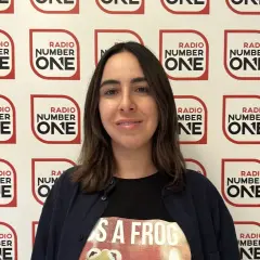 Federica Abbate, con una maglietta a tema rana, sorride davanti a uno sfondo con il logo di Radio Number One. Le sue canzoni risuonano in radio.