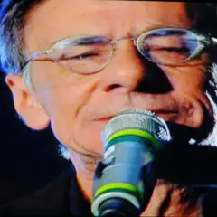 Roberto Vecchioni canta "Chiamami ancora amore" con passione, il microfono vicino alle labbra, sullo sfondo verde di Rai 1.