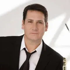 Tony Hadley, uno dei membri dei Spandau Ballet, in giacca e cravatta, con un microfono sullo sfondo.