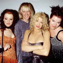 Il gruppo musicale Hole posa sorridendo. Courtney Love al centro, con i capelli biondi e un vestito scuro.