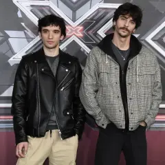 I **santi francesi** posano davanti al logo di X Factor. Uno indossa un chiodo di pelle nera, l'altro una giacca a quadri.