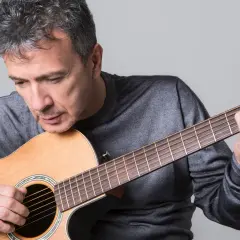 Uomo con chitarra acustica, intento a suonare, forse componendo nuove canzoni di pupo.