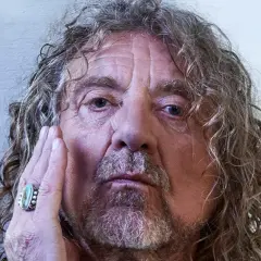 Primo piano di Robert Plant, con la mano sul viso, un anello turchese. La sua espressione è intensa, quasi una saving grace per chi lo osserva.