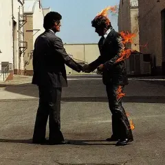 Due uomini si stringono la mano, uno in fiamme. Un'immagine iconica che evoca il "wish you were here significato" di assenza e desiderio.