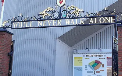 L'iconico cancello di Anfield con la scritta "You'll Never Walk Alone" e lo stemma del Liverpool. Un simbolo di unità e passione.