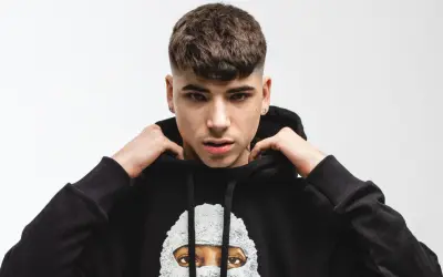 Giovane rapper italiano con un taglio di capelli alla moda, indossa una felpa nera con un disegno artistico.
