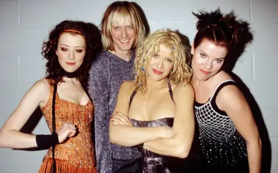 Il gruppo musicale Hole posa sorridendo. Courtney Love al centro, con i capelli biondi e un vestito scuro.