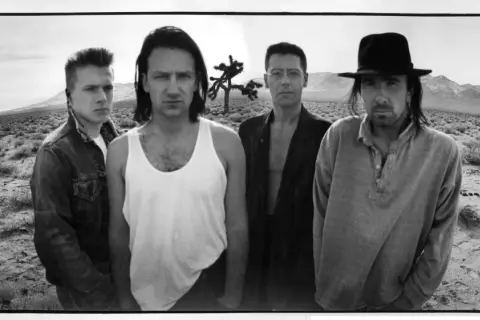 I membri degli U2 posano in un paesaggio desertico, con un Joshua Tree sullo sfondo.