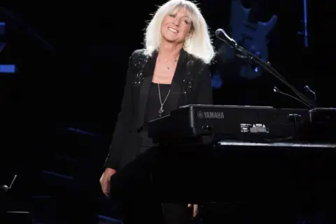 La cantante dei Fleetwood Mac, con i capelli biondi sciolti, sorride dietro una tastiera Yamaha.