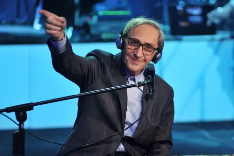 Franco Battiato, con cuffie e microfono, indica con il dito, come in un "auto da fé" di parole.