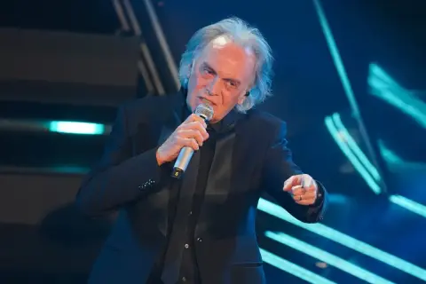 Riccardo Fogli canta sul palco, con il microfono in mano, evocando le sue indimenticabili canzoni.