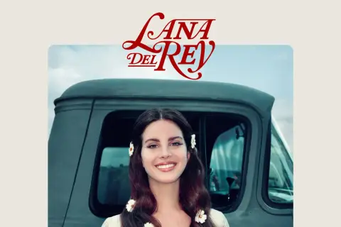 Lana Del Rey sorride, con fiori tra i capelli, accanto a un vecchio camion. Un'immagine che evoca il suo "lust for life".