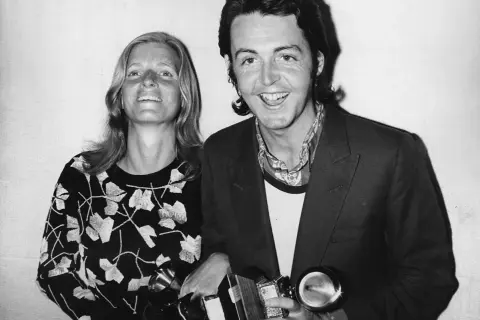 Paul McCartney sorride con una donna, entrambi tengono premi. Potrebbe essere un momento legato a un album di Paul McCartney.