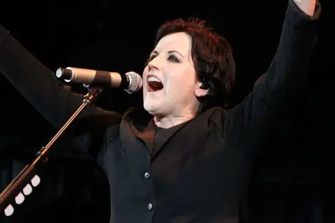 Dolores O'Riordan, iconica voce dei The Cranberries, canta con passione sul palco, braccia alzate in un momento di pura energia.