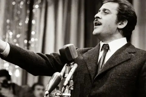 Domenico Modugno, originario di Polignano a Mare, canta con passione al microfono, con il braccio teso.