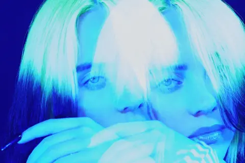 Billie Eilish, icona del pop alternativo, con capelli verdi e blu, in un'immagine surreale che evoca il suo genere musicale unico.