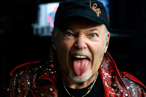 Vasco Rossi, con la lingua fuori e un'espressione grintosa, indossa una giacca borchiata. Chissà quante canzoni ha fatto Vasco Rossi per arrivare a tanta energia!