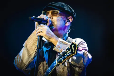 Luca Carboni canta "Le storie d'amore" con passione, chitarra in mano, sotto le luci del palco.