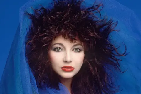 Ritratto di Kate Bush con capelli scuri e fluenti, occhi verdi penetranti e labbra rosse, avvolta in un velo blu. Un'icona delle canzoni di Kate Bush.