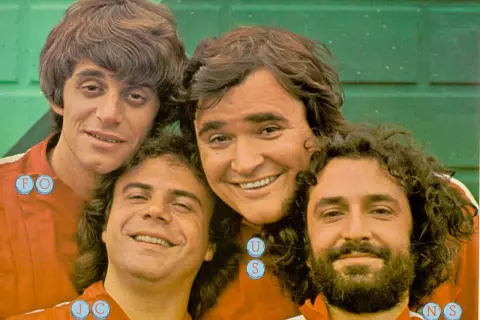 I gatti di Vicolo Miracoli sorridono alla telecamera, un gruppo di amici con capelli mossi e barbe folte.