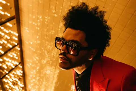 The Weeknd, con occhiali oversize e giacca rossa, pronto per le avventure after hours.