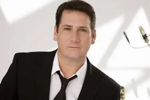 Tony Hadley, uno dei membri dei Spandau Ballet, in giacca e cravatta, con un microfono sullo sfondo.