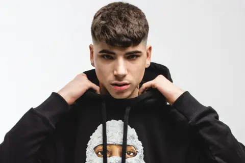 Giovane rapper italiano con un taglio di capelli alla moda, indossa una felpa nera con un disegno artistico.