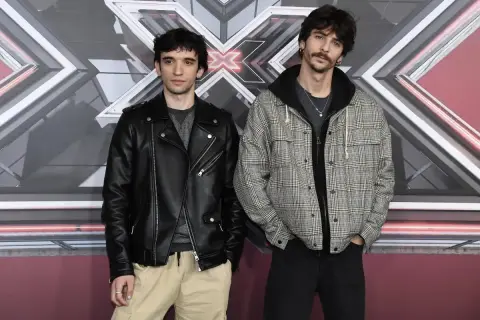 I **santi francesi** posano davanti al logo di X Factor. Uno indossa un chiodo di pelle nera, l'altro una giacca a quadri.
