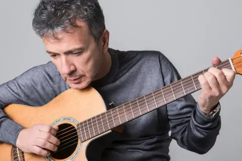 Uomo con chitarra acustica, intento a suonare, forse componendo nuove canzoni di pupo.