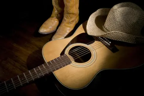 Stivali da cowboy, cappello di paglia e chitarra acustica, pronti per suonare le più belle canzoni country famose.