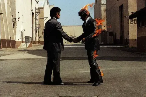 Due uomini si stringono la mano, uno in fiamme. Un'immagine iconica che evoca il "wish you were here significato" di assenza e desiderio.